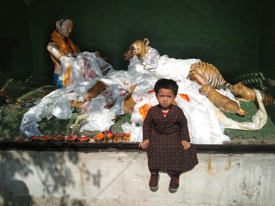 Un enfant en vêtements traditionnels devant une statue et une œuvre d'art représentant un tigre.