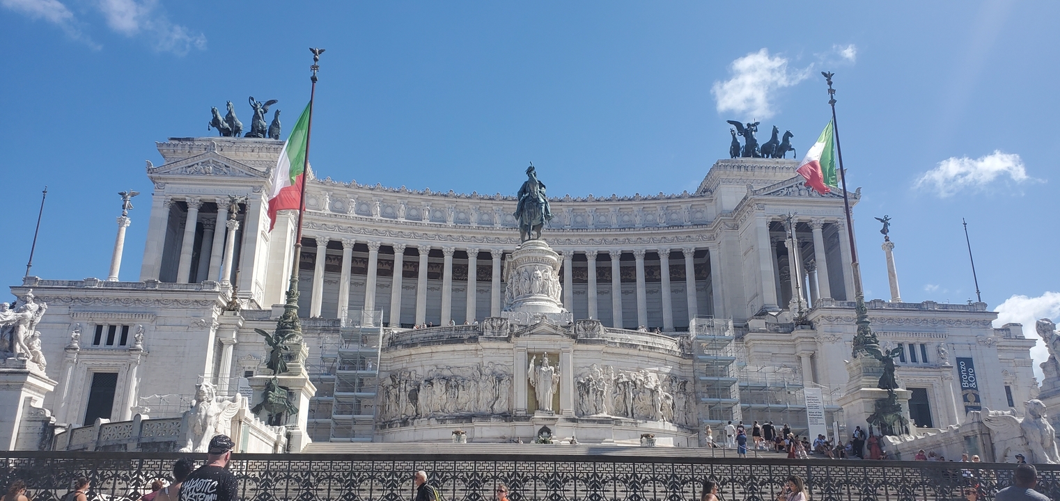 Bâtiment monumental avec colonnes et drapeaux italiens.