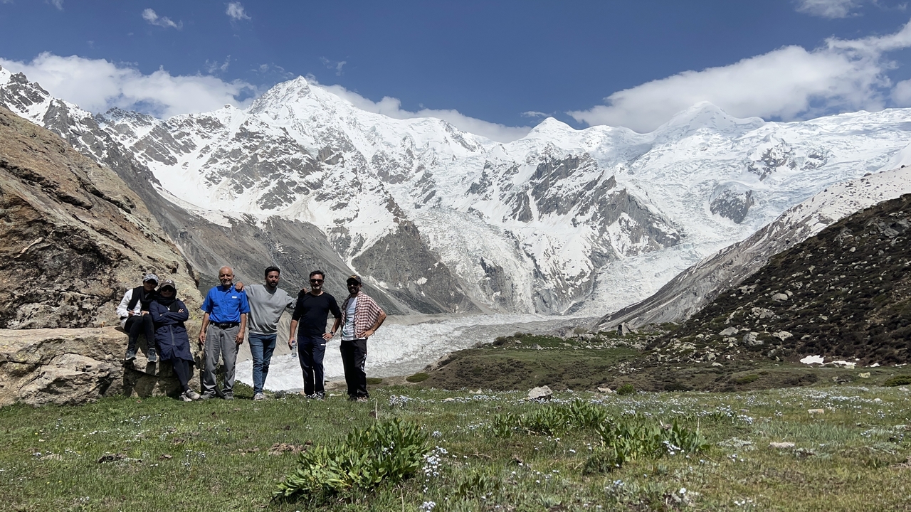 Groupe de personnes debout sur l'herbe avec des montagnes enneigées en arrière-plan.
