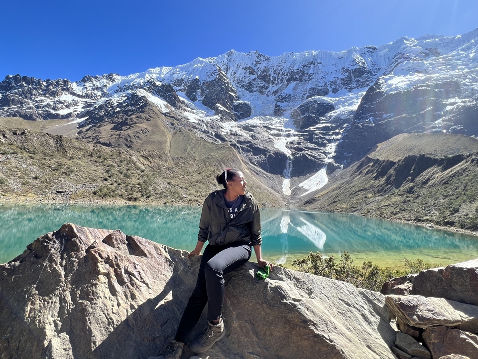Personne assise devant un lac turquoise et des montagnes enneigées.