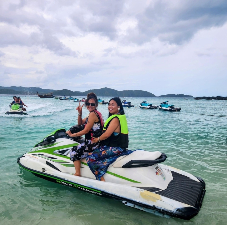 Deux femmes sur un jet-ski dans des eaux claires avec d'autres jet-skis en arrière-plan.