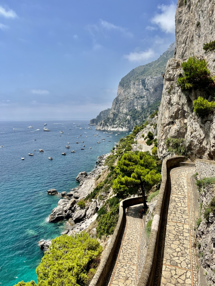 Sentier le long d'une côte rocheuse avec vue sur plusieurs bateaux en mer.