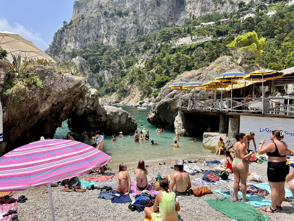 Plage avec des gens qui nagent et se détendent près d'une entrée rocheuse.