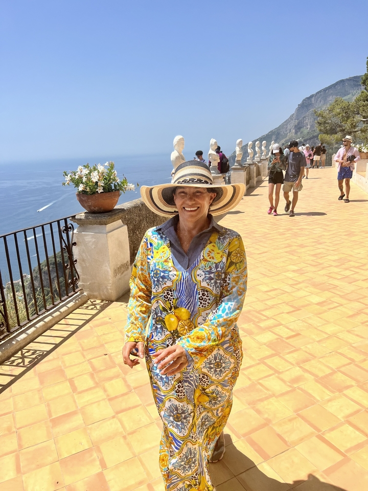 Personne souriante en tenue colorée debout sur une terrasse carrelée avec vue sur la mer.