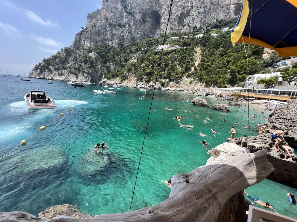 Plage avec des gens qui nagent et se détendent, entourée de falaises rocheuses.