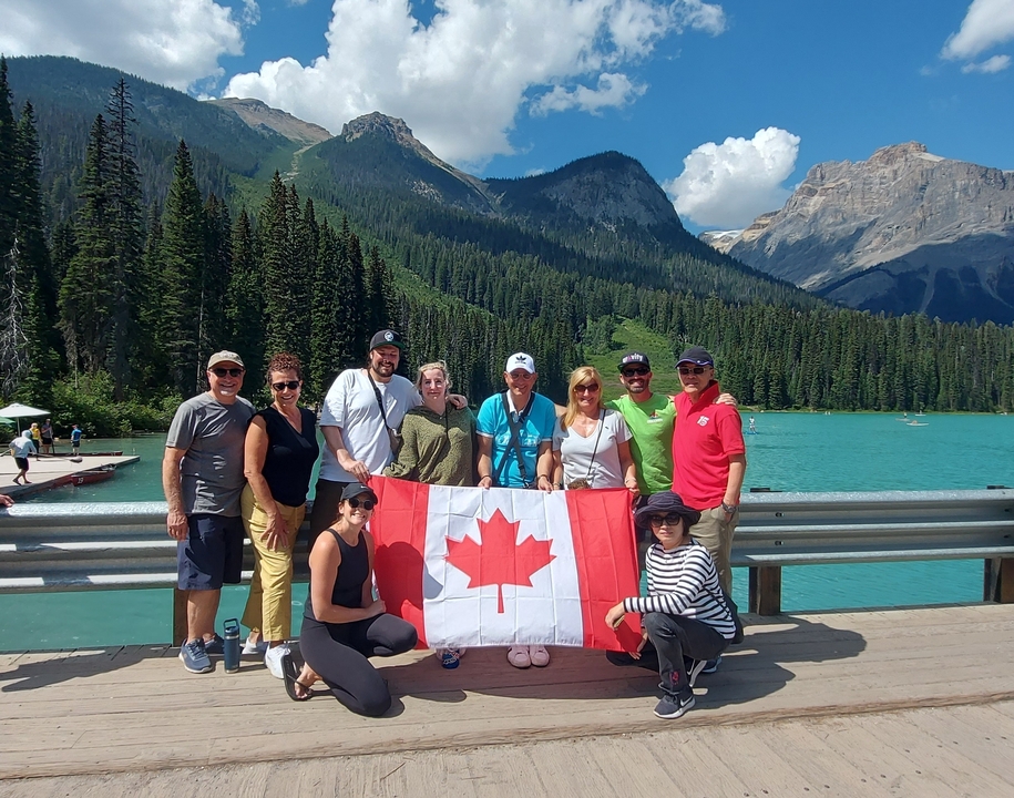 Groupe de personnes tenant un drapeau canadien près d'un lac dans les montagnes.