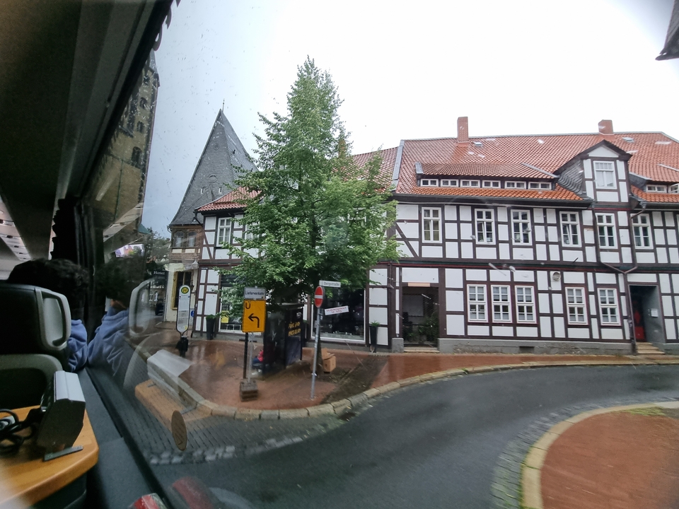 Une vue depuis un bus d'un bâtiment traditionnel à colombages et d'une rue bordée d'arbres.