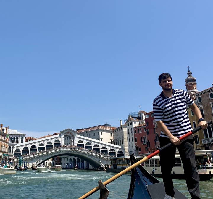 Gondolier rowing a gondola with Rialto Bridge in the background.