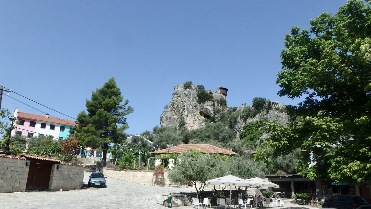 Place du village avec une colline rocheuse et une tour en arrière-plan.