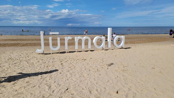 Beach with 'Jurmala' sign, people enjoying the sunny day.