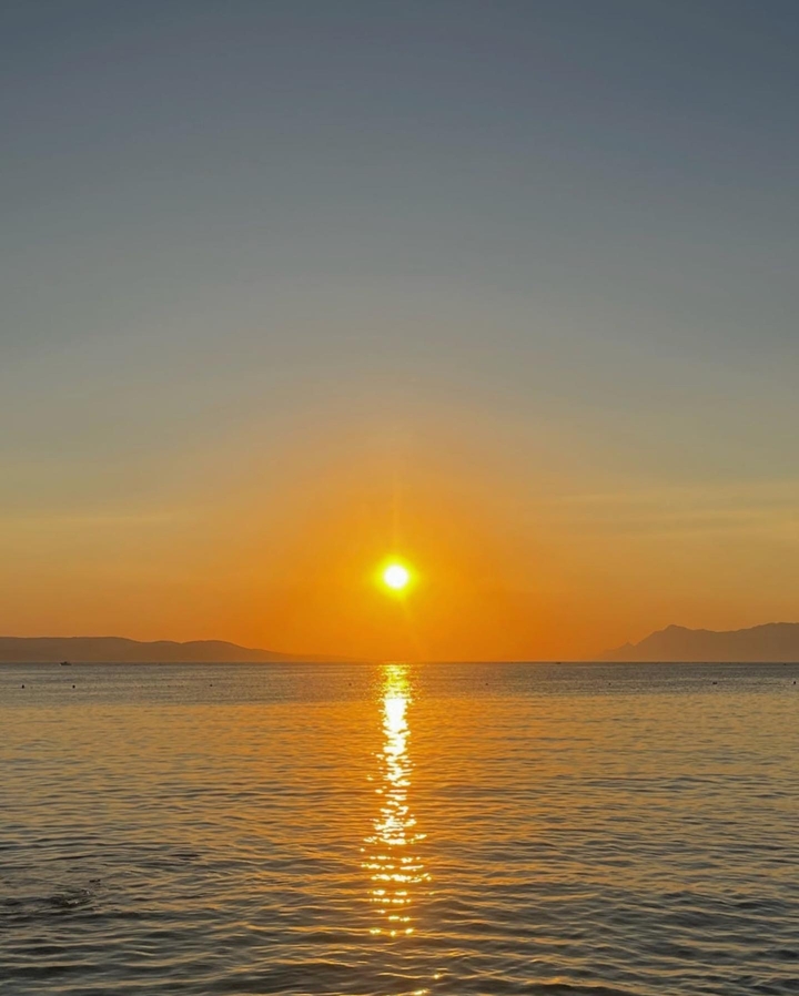 Un coucher de soleil doré sur la mer avec des montagnes lointaines.