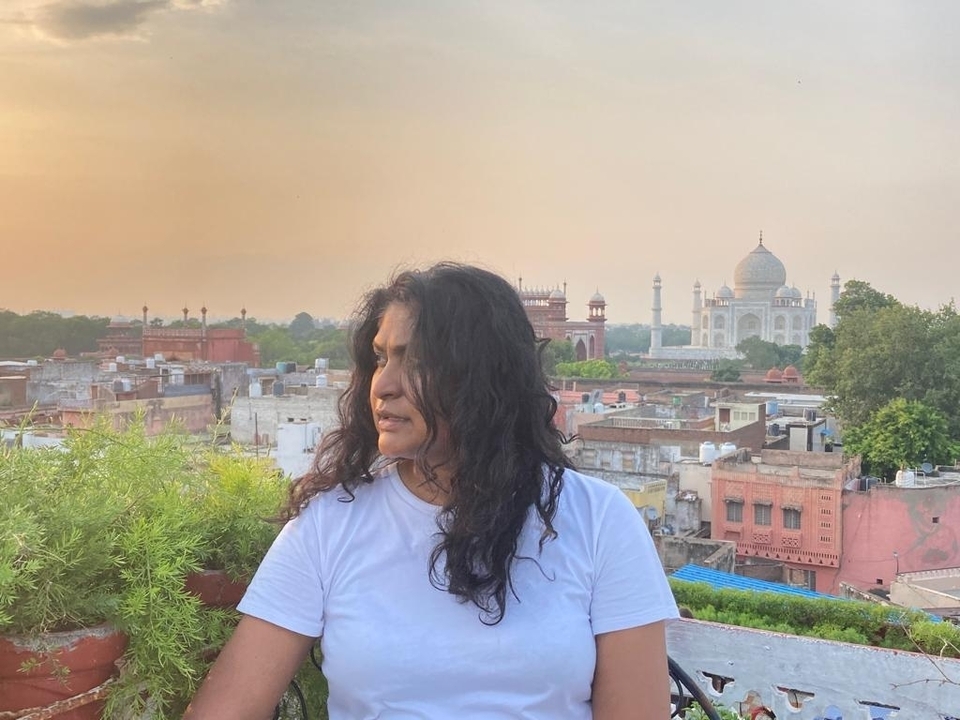 Femme sur un balcon avec une vue lointaine du Taj Mahal au coucher du soleil.