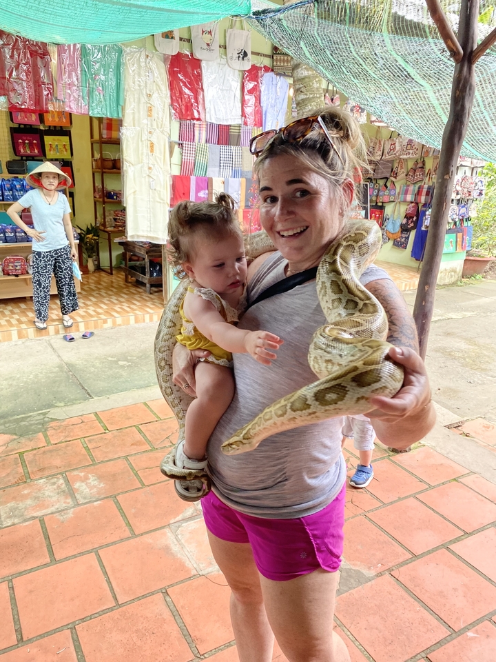 Personne tenant un serpent avec un bambin qui observe.