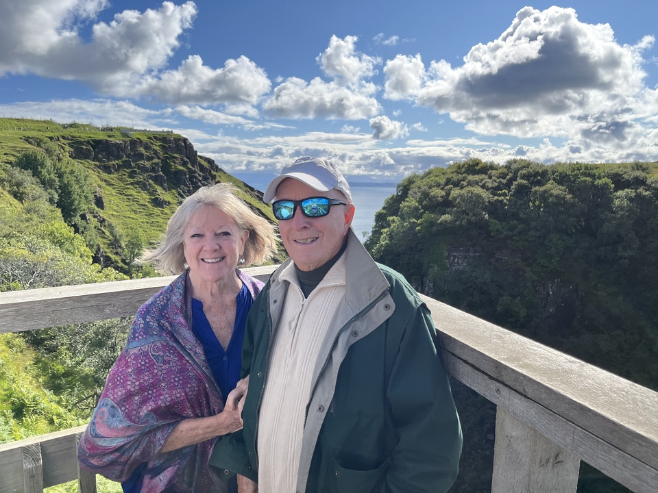Couple smiling with a scenic view of cliffs and sea.