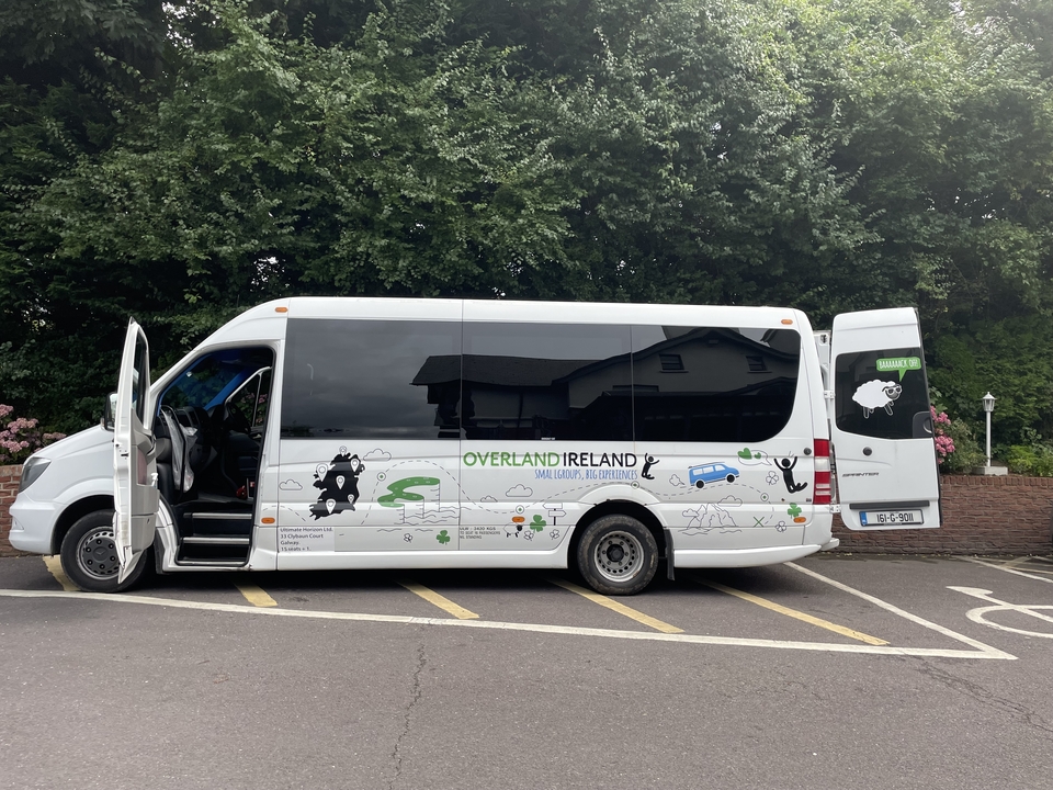 Bus touristique avec la marque 'Overland Ireland' garé dans un parking.