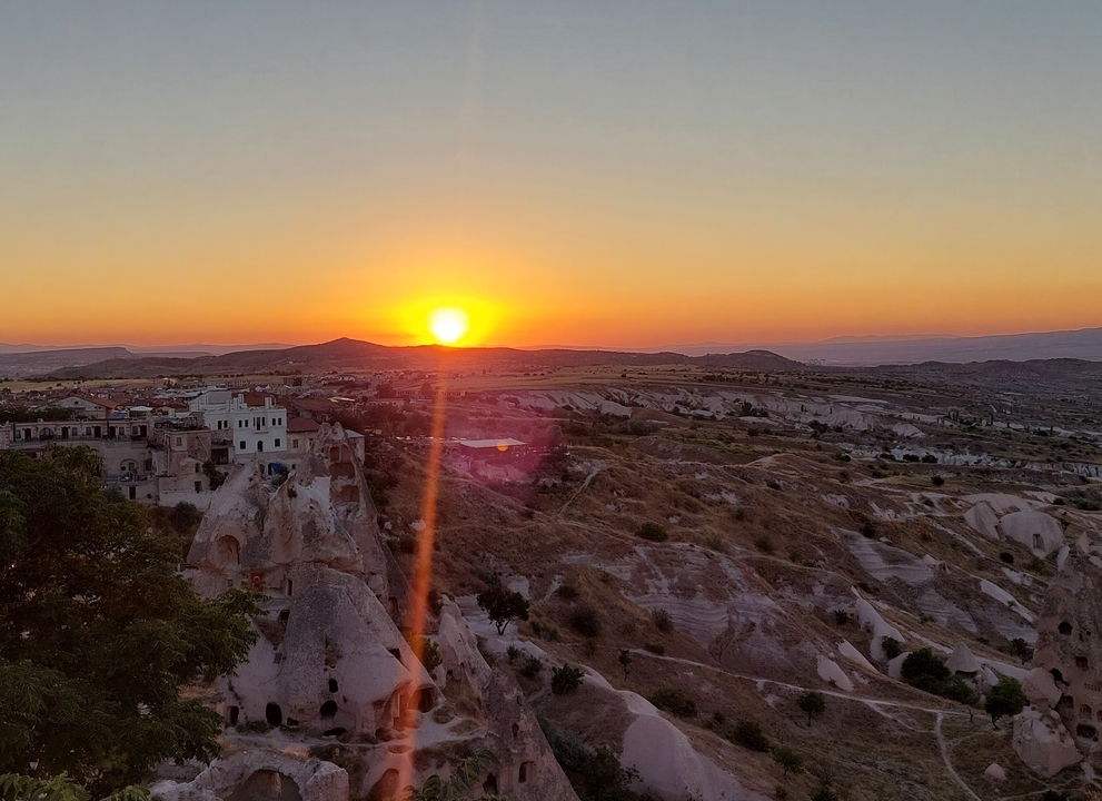 Coucher de soleil sur un paysage accidenté avec des bâtiments au loin.