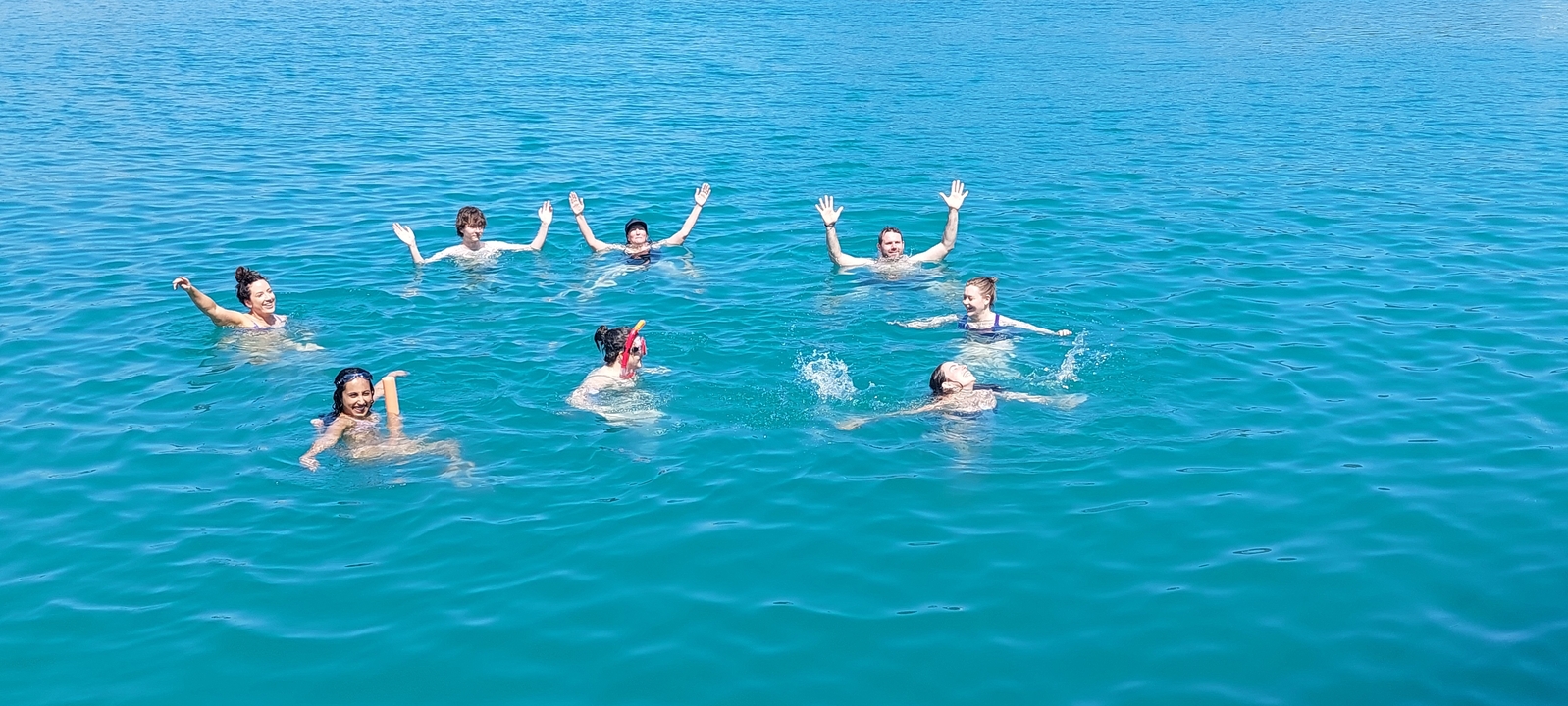 Groupe de personnes nageant dans l'océan, saluant de la main vers la caméra.