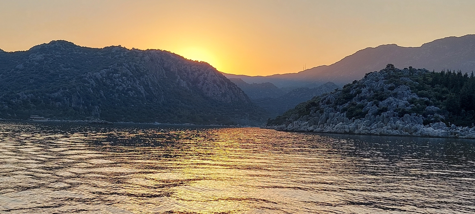 Soleil couchant sur les montagnes et se reflétant sur l'eau.