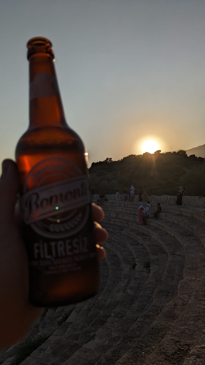 Des gens assis sur d'anciens escaliers de pierre avec une bouteille de bière au premier plan.