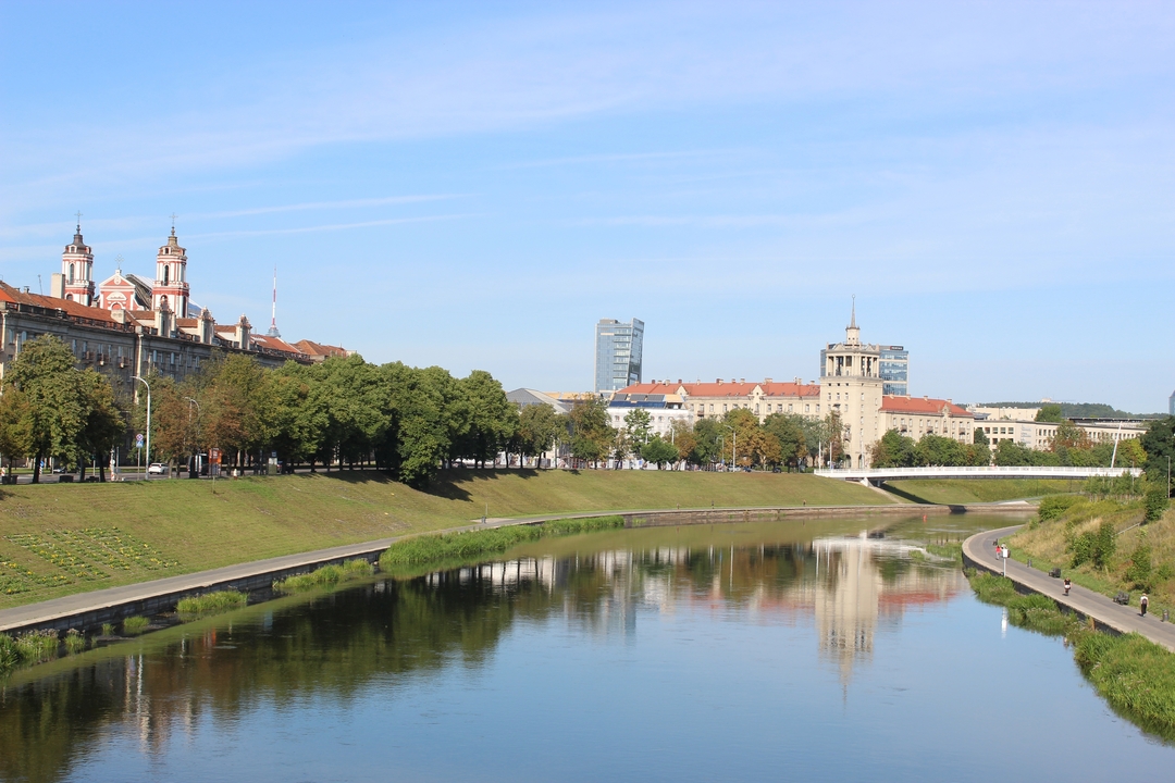 Paysage urbain avec rivière reflétant les bâtiments et ciel dégagé.