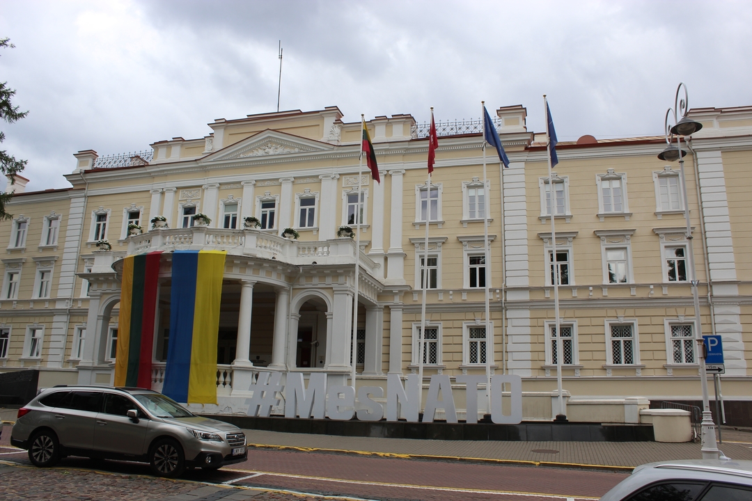 Bâtiment historique avec des drapeaux et un panneau #MesNato.