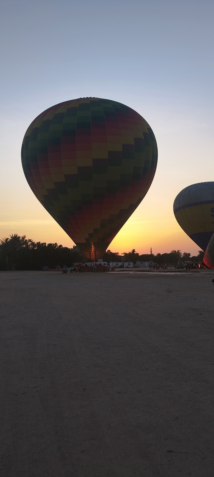 Hot air balloons on the ground with the sun setting in the background.