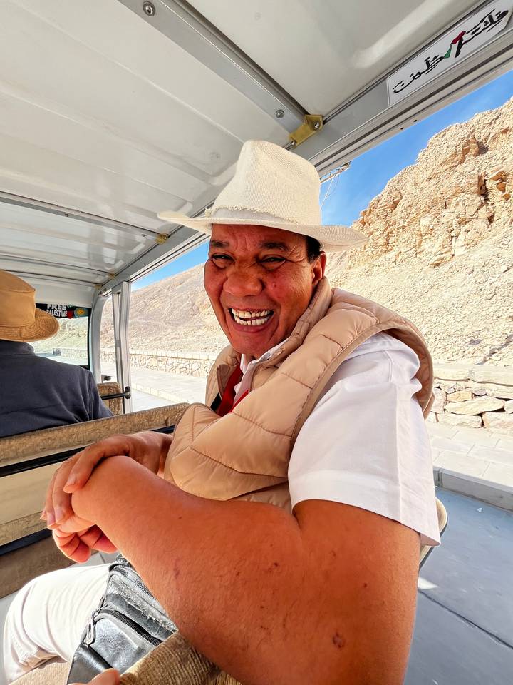 Une personne souriante à l'intérieur d'un véhicule avec un paysage rocheux en arrière-plan.