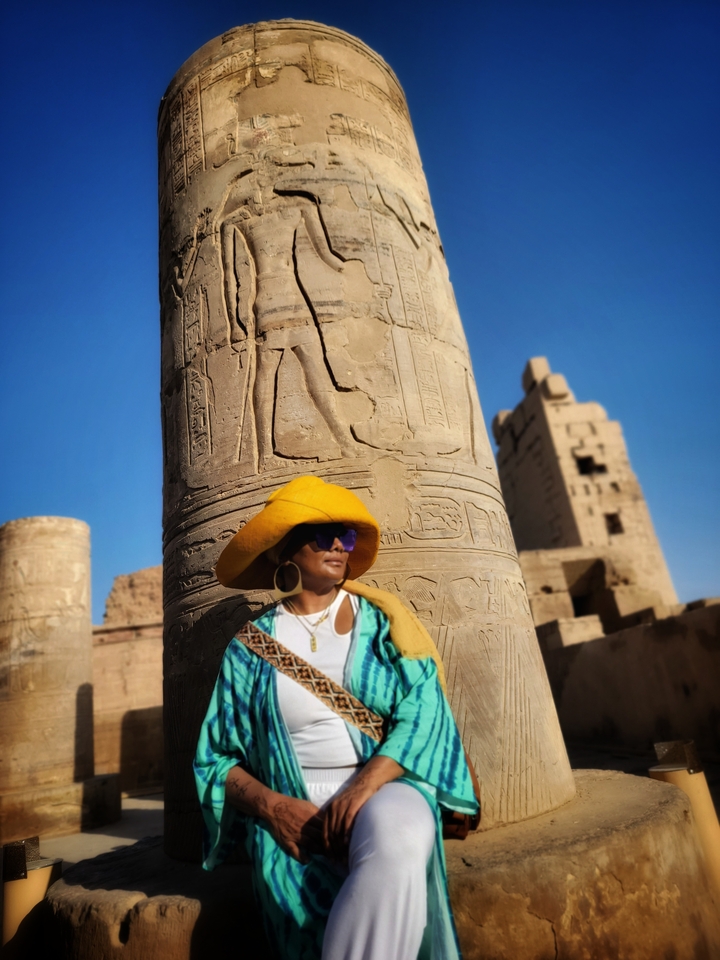 Person in front of ancient Egyptian ruins with intricate carvings.