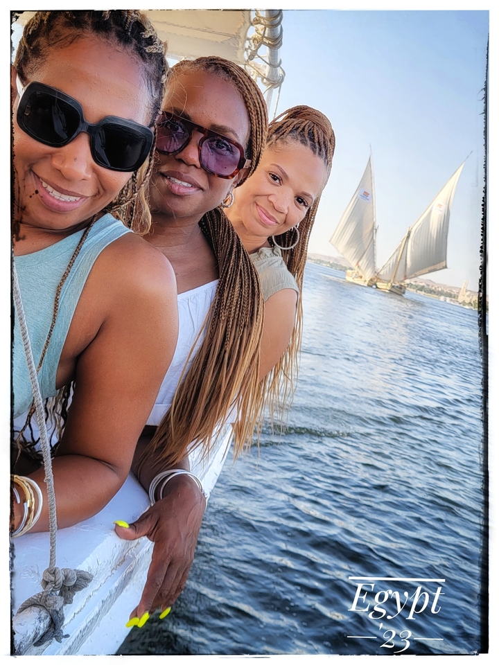 Three women posing with a river and sailboats in the background, photo has a frame effect.