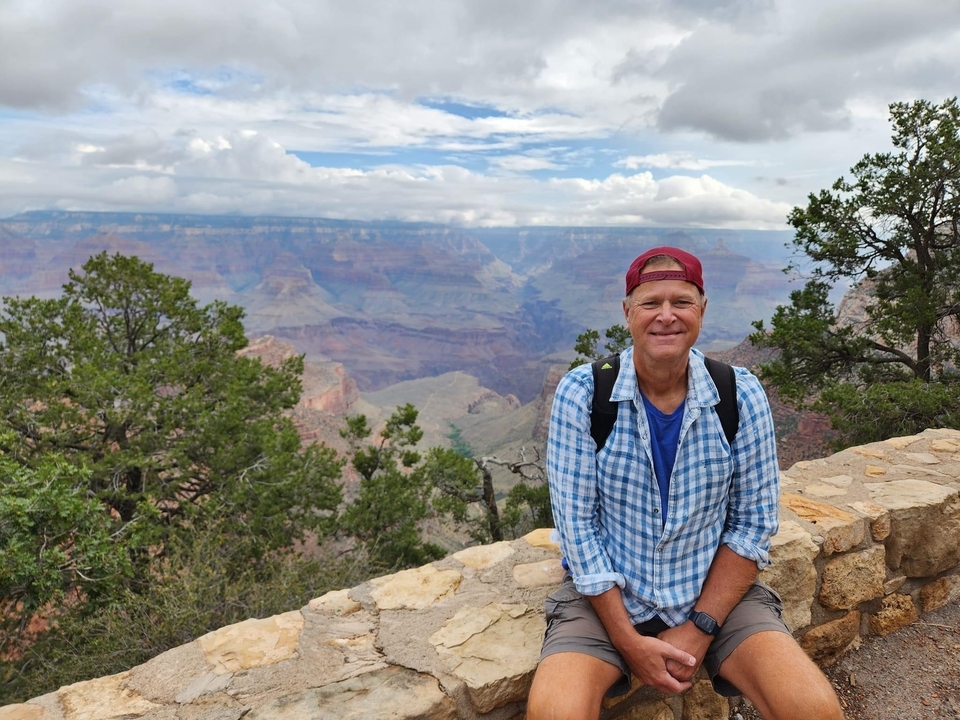 Une personne assise sur un mur de pierre avec une vue du Grand Canyon en arrière-plan.