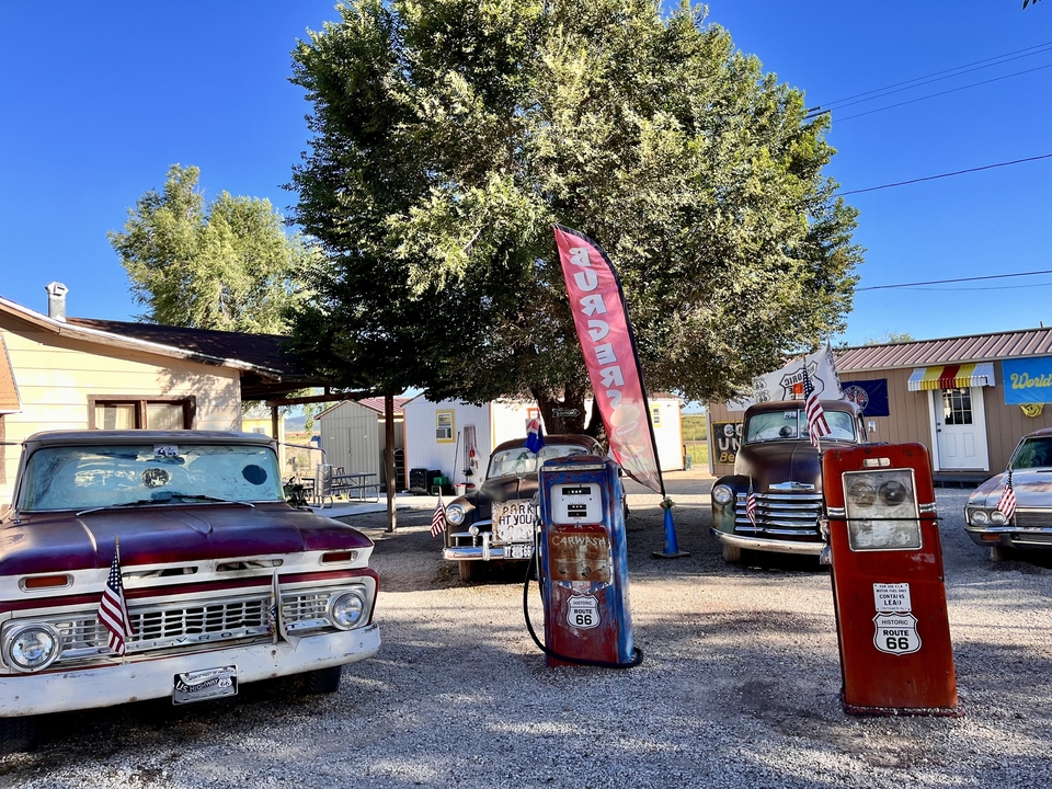 Collection de voitures classiques et de pompes à essence vintage dans un aménagement en bord de route.