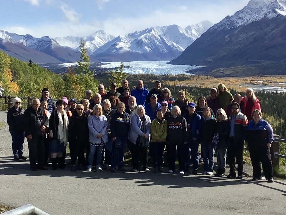 Un grand groupe posant avec un glacier et des montagnes en arrière-plan.