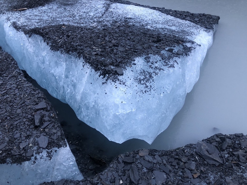 Gros plan d'un morceau de glacier bleu sur un sol rocheux.