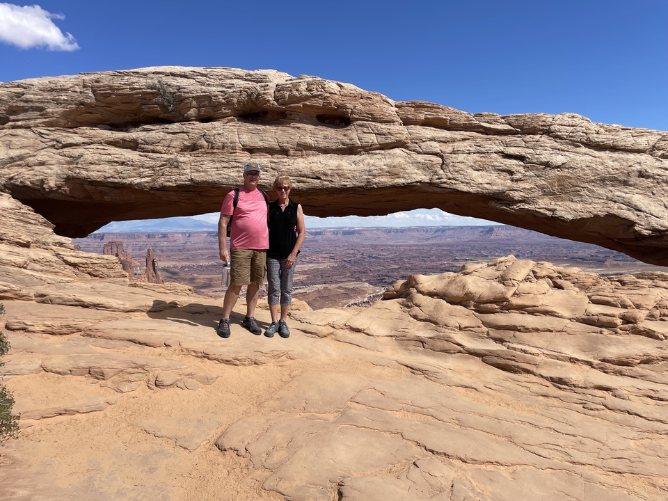 Deux personnes debout sous une arche naturelle avec un paysage étendu.