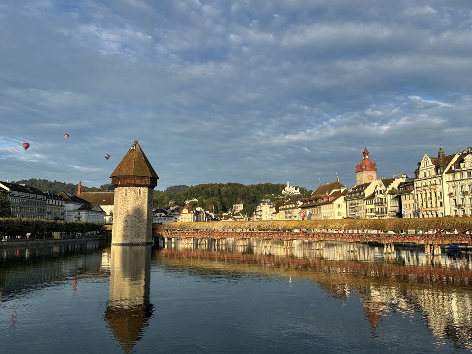 Bâtiment historique avec reflet dans l'eau et montgolfières.