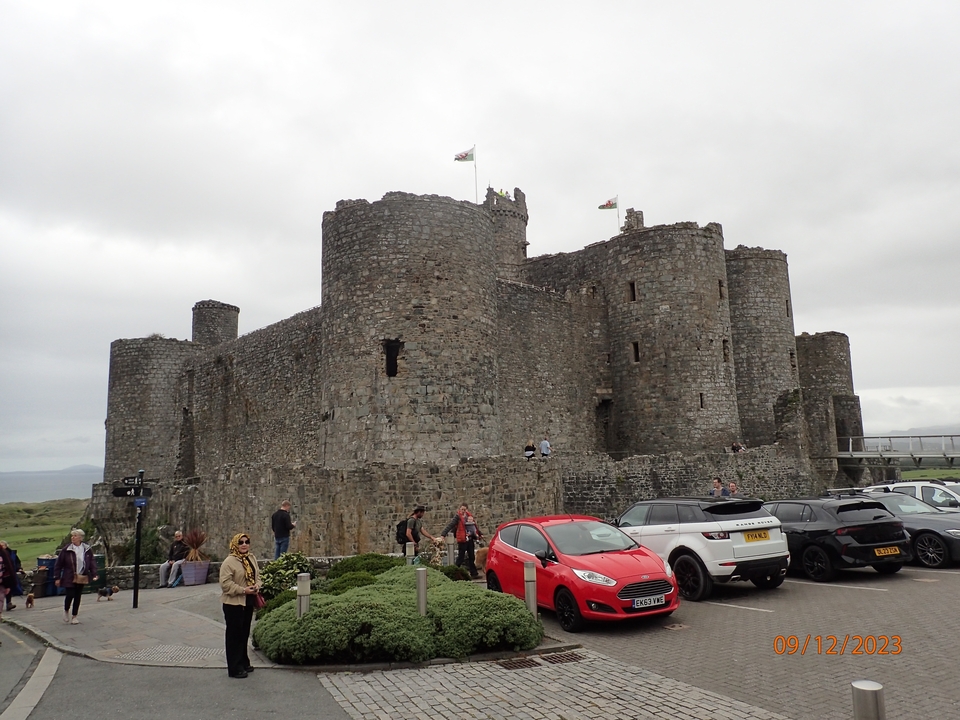 Un château avec des drapeaux gallois, des gens et des voitures devant.