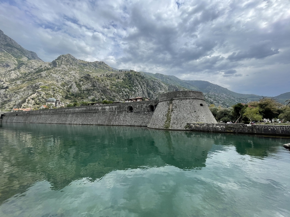 Forteresse historique au bord d'une rivière turquoise sous un ciel nuageux.