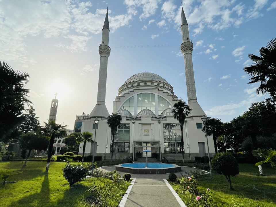 Mosquée blanche moderne avec deux minarets jumeaux et soleil couchant derrière.