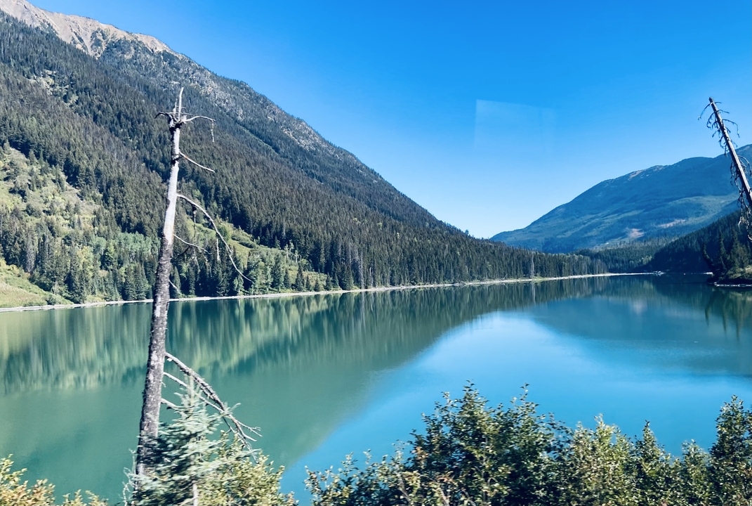 Lac serein entouré de montagnes boisées sous un ciel dégagé.