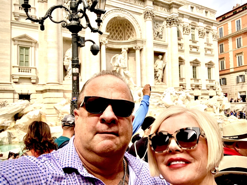 Deux personnes qui prennent un selfie devant une fontaine historique avec une maçonnerie complexe.