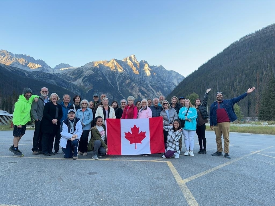 Groupe de personnes tenant un drapeau canadien dans une région montagneuse.