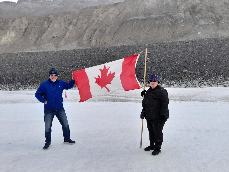 Deux personnes tenant un drapeau canadien sur une surface enneigée.