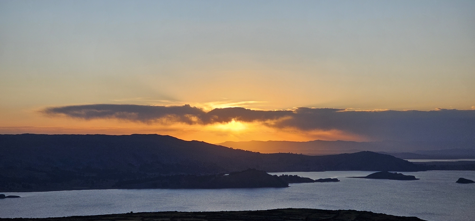 Vue de coucher de soleil sur un lac avec des îles et des montagnes en silhouette.