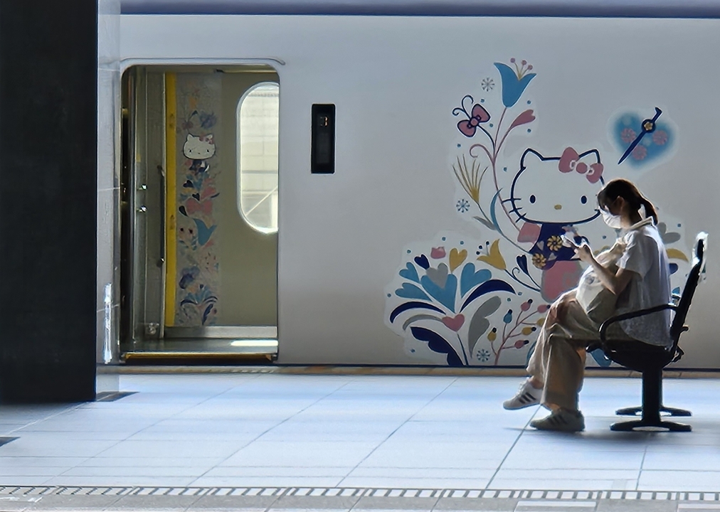 Personne assise dans une gare avec un train décoré artistiquement en arrière-plan.