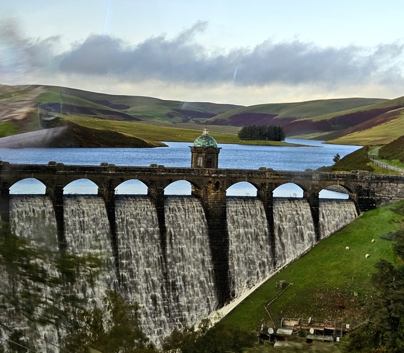 Réservoir avec un barrage voûté entouré de collines.