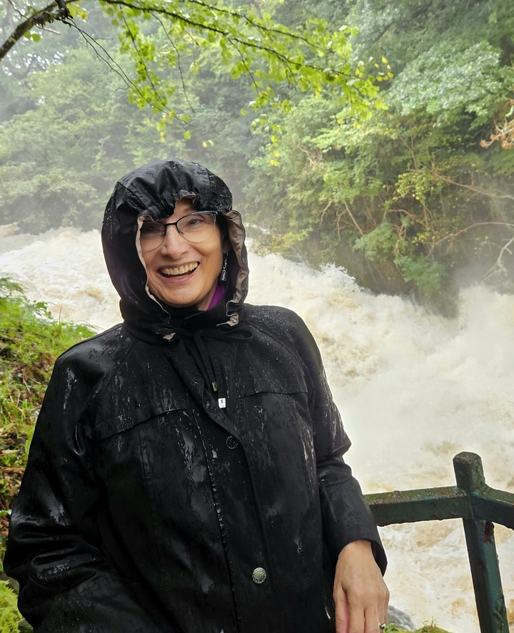Femme souriante devant une cascade par jour de pluie.