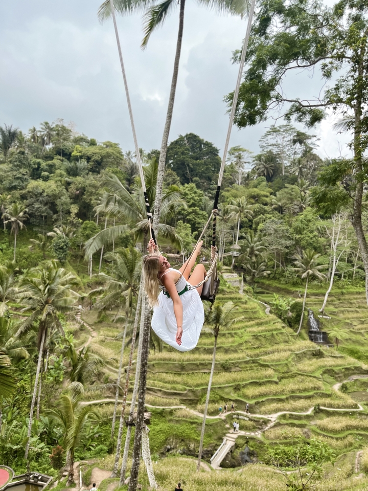 Femme sur une balançoire au-dessus d'un paysage tropical.