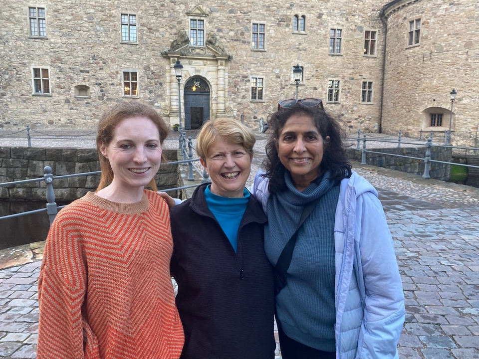 Trois femmes posant devant un bâtiment historique en pierre.