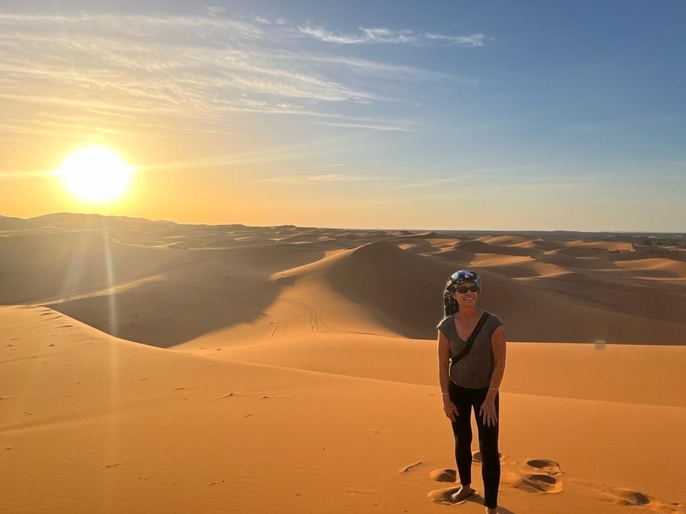 Eine Person, die bei Sonnenuntergang auf Sanddünen steht, während die Sonne über der Wüste untergeht.