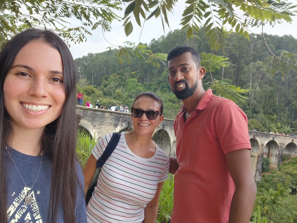 Trois personnes prenant un selfie avec un pont de pierre en arrière-plan.